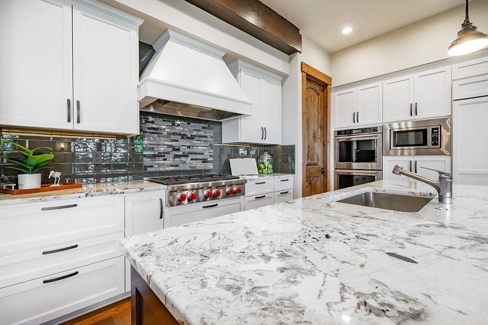 A kitchen with white cabinets , granite counter tops , and stainless steel appliances.
