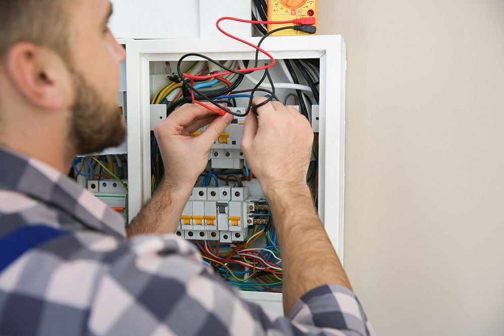 A man is working on an electrical box with a multimeter.