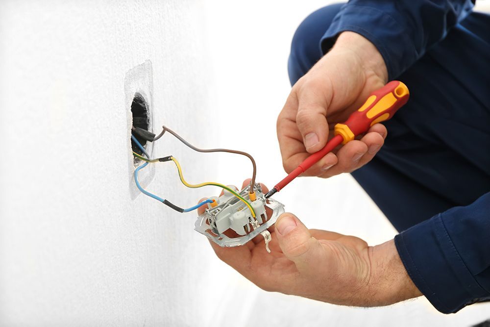 A man is fixing an electrical outlet with a screwdriver