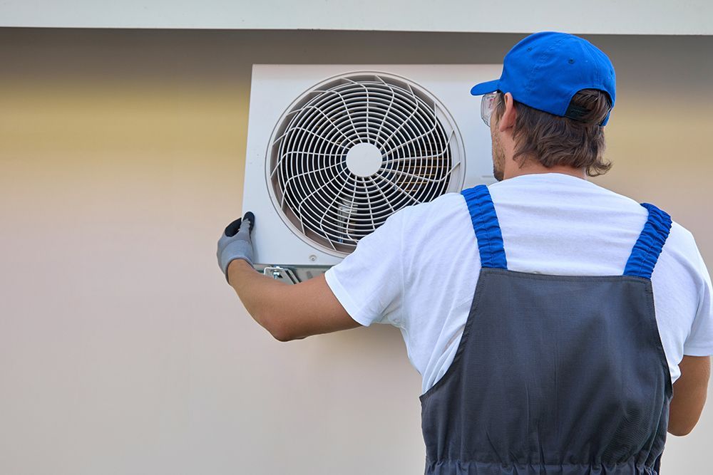 A man is installing an air conditioner on the side of a building.