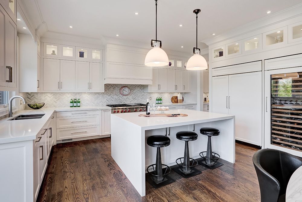 A kitchen with white cabinets , hardwood floors , and a large island.