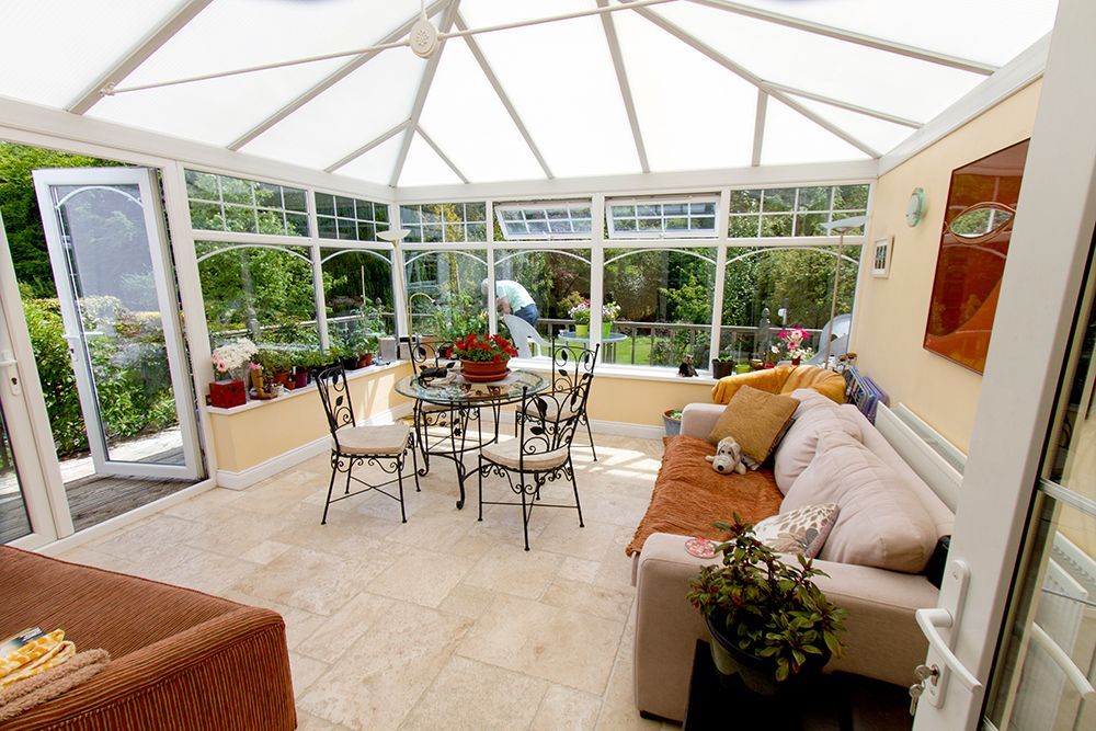 A living room with a couch , table and chairs in a conservatory.