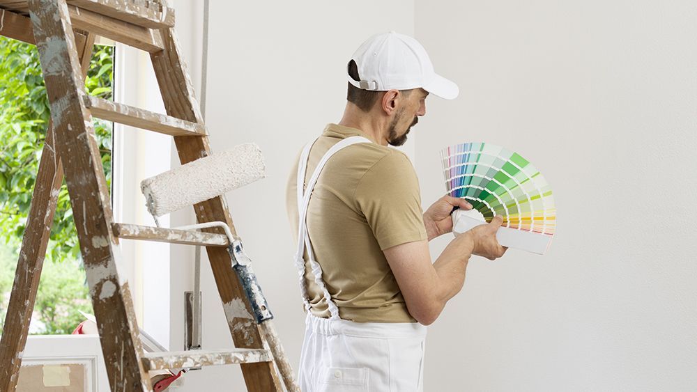 A man is standing next to a ladder holding a palette of paint.