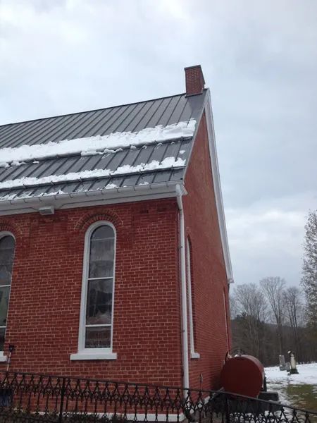 Red brick church with dark roof and snow, overcast sky.