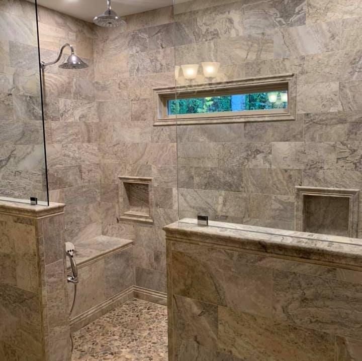 Bathroom shower with stone walls, pebble floor, bench, glass enclosure, and window.