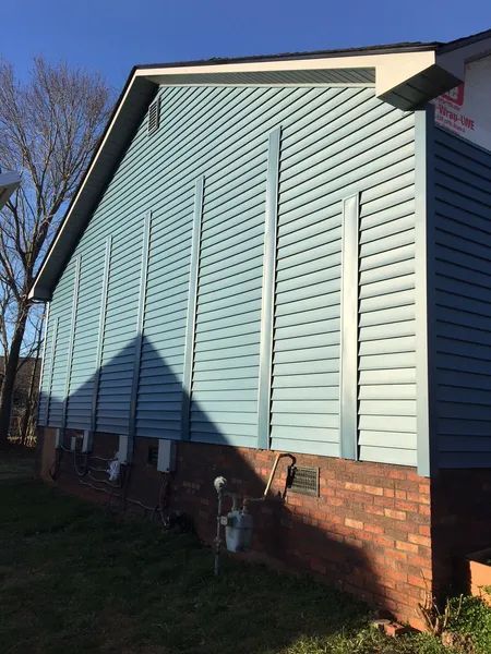 Light blue siding on a house with vertical metal flashing strips. Brick foundation. Sunny day.