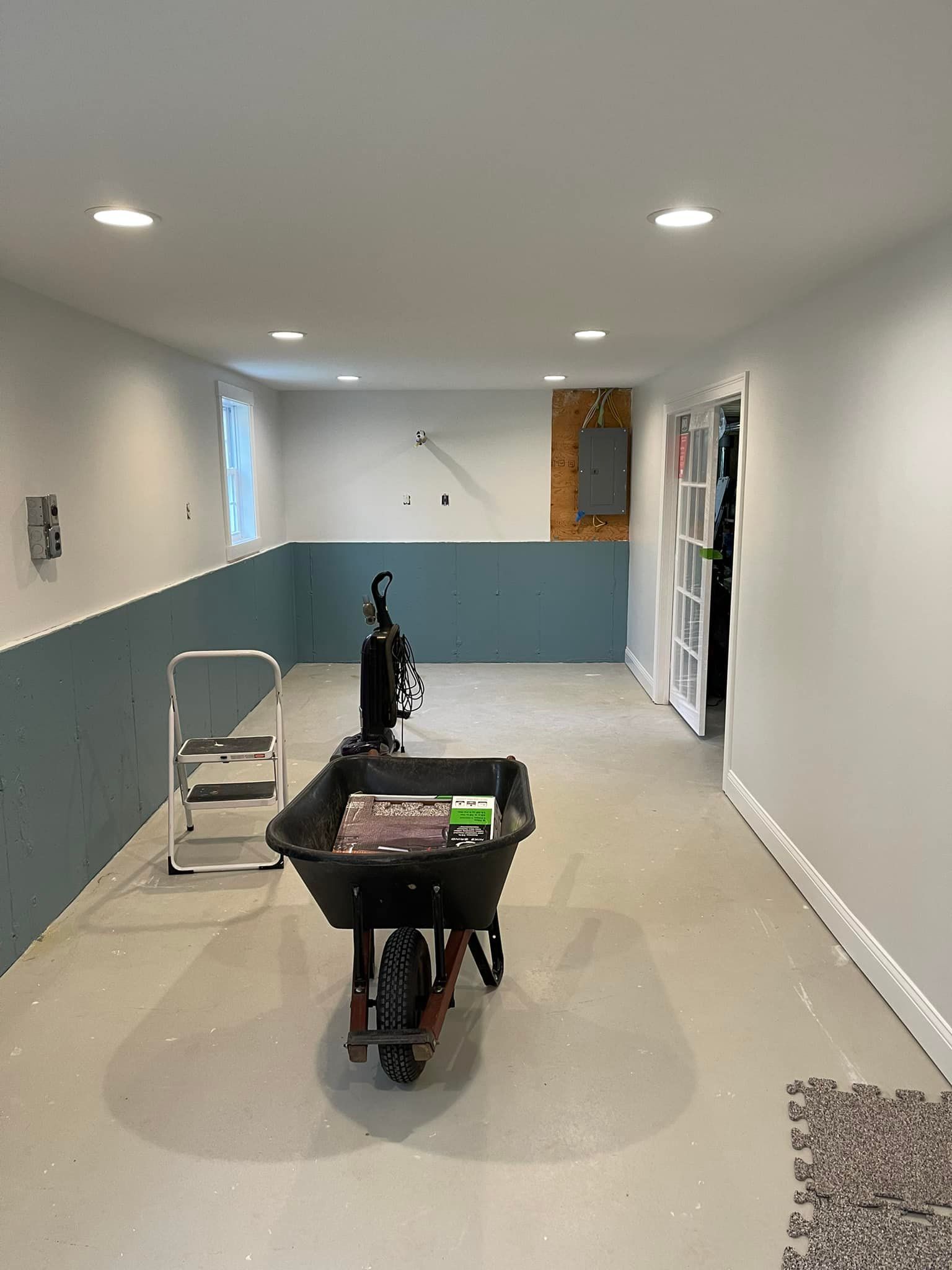 Basement room with blue wainscoting, wheelbarrow, and a step ladder.