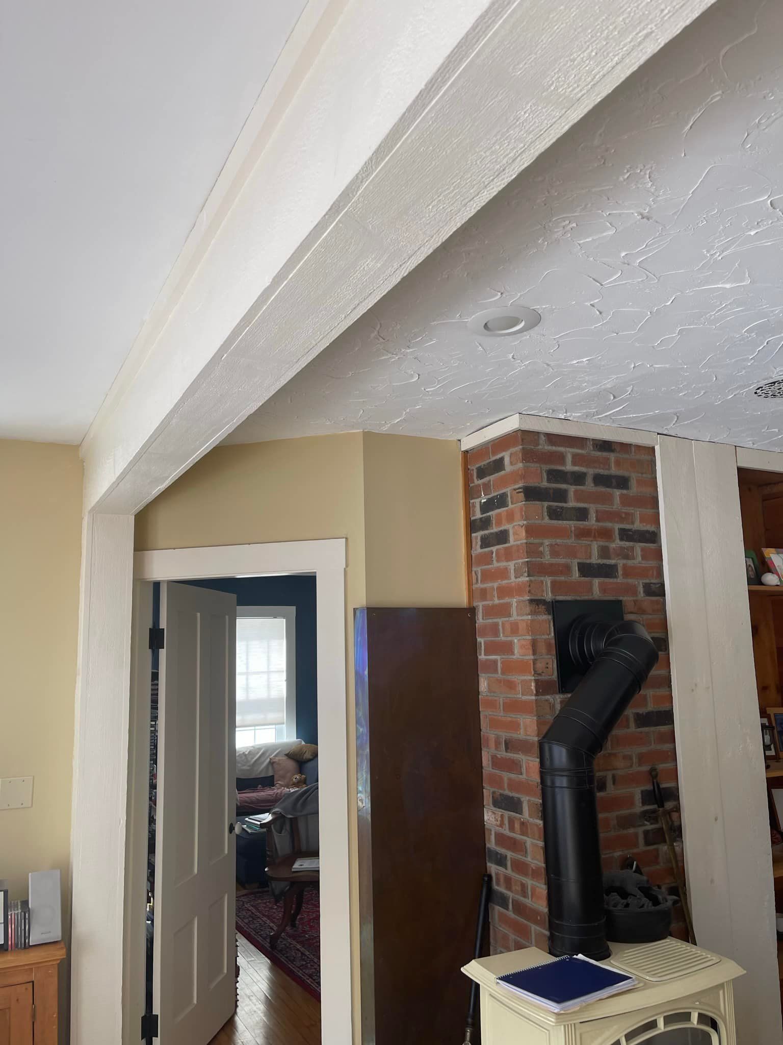 Interior view of a home: doorway, fireplace, textured beam, tan wall, white trim, and a hint of an open door to a room.