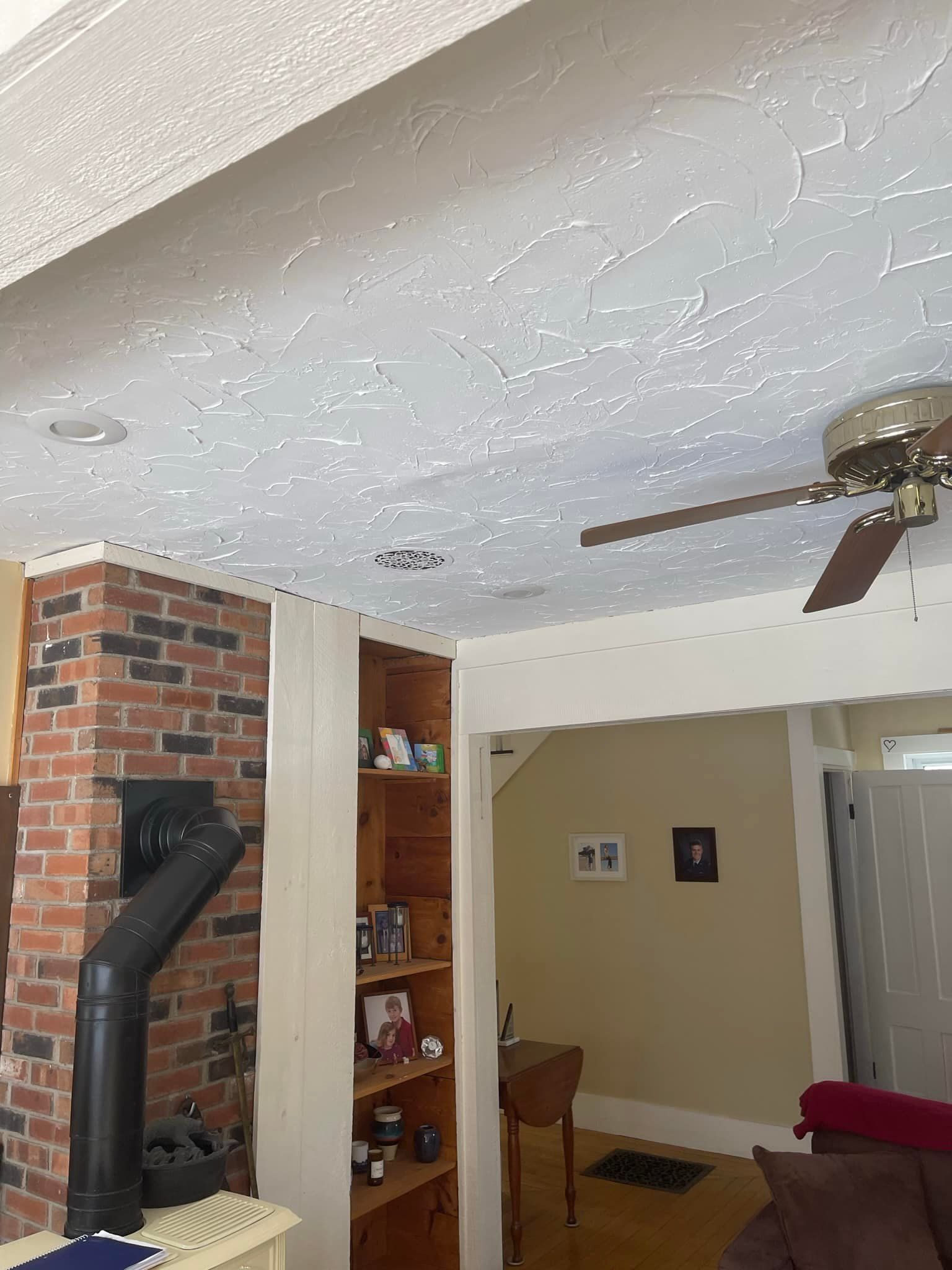 Living room interior with a brick fireplace, built-in shelving, ceiling fan, and doorway to another room.