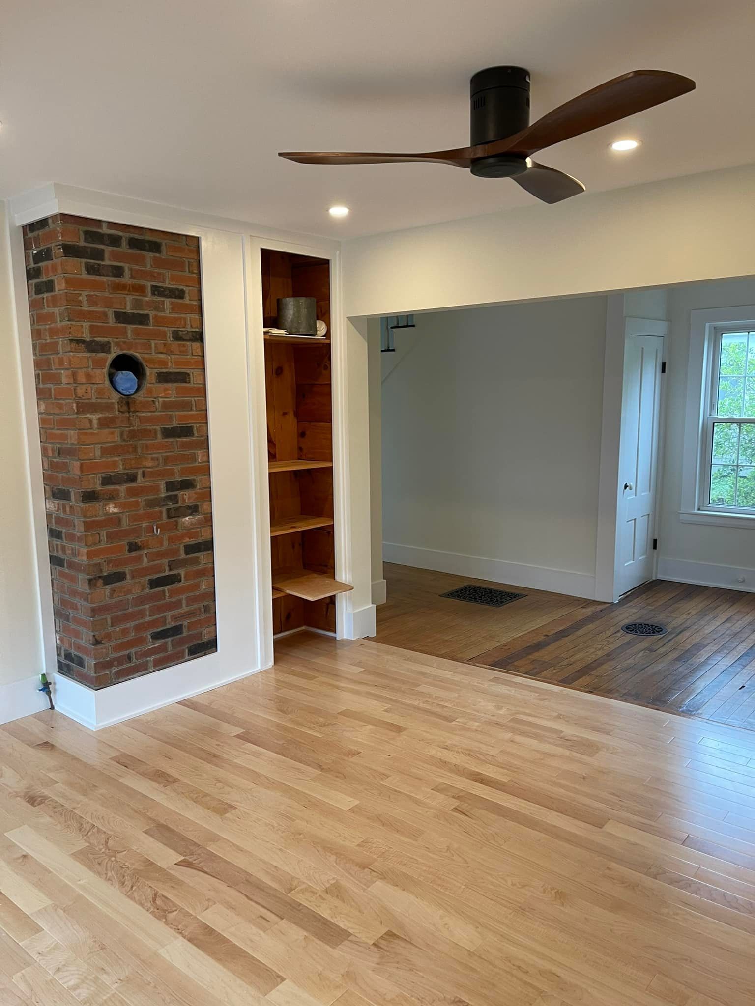 Living room with brick chimney, wooden shelves, hardwood floors, and ceiling fan.