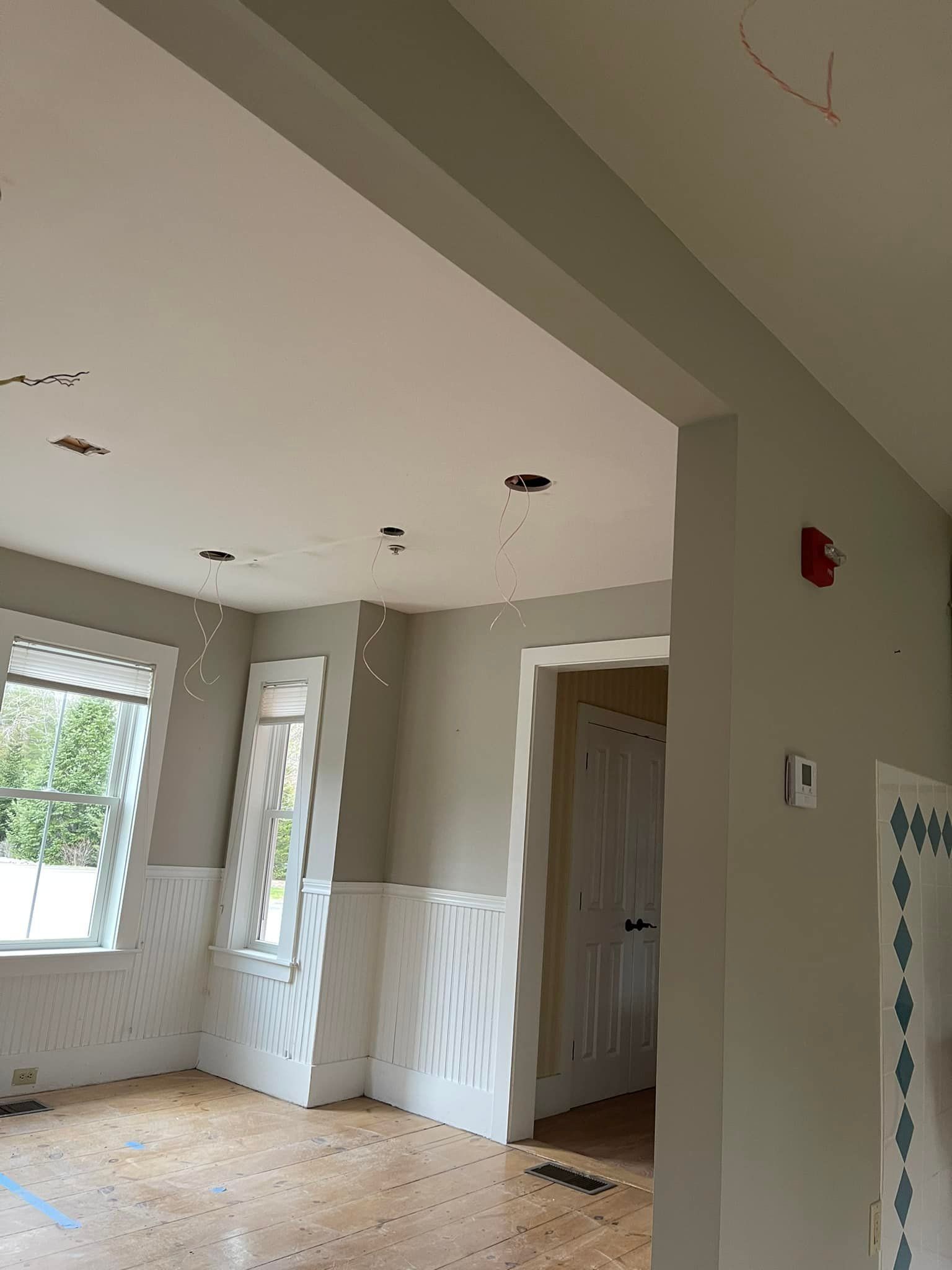 Interior view of a room with light gray walls, wood floors, and white trim. A doorway leads to another room.
