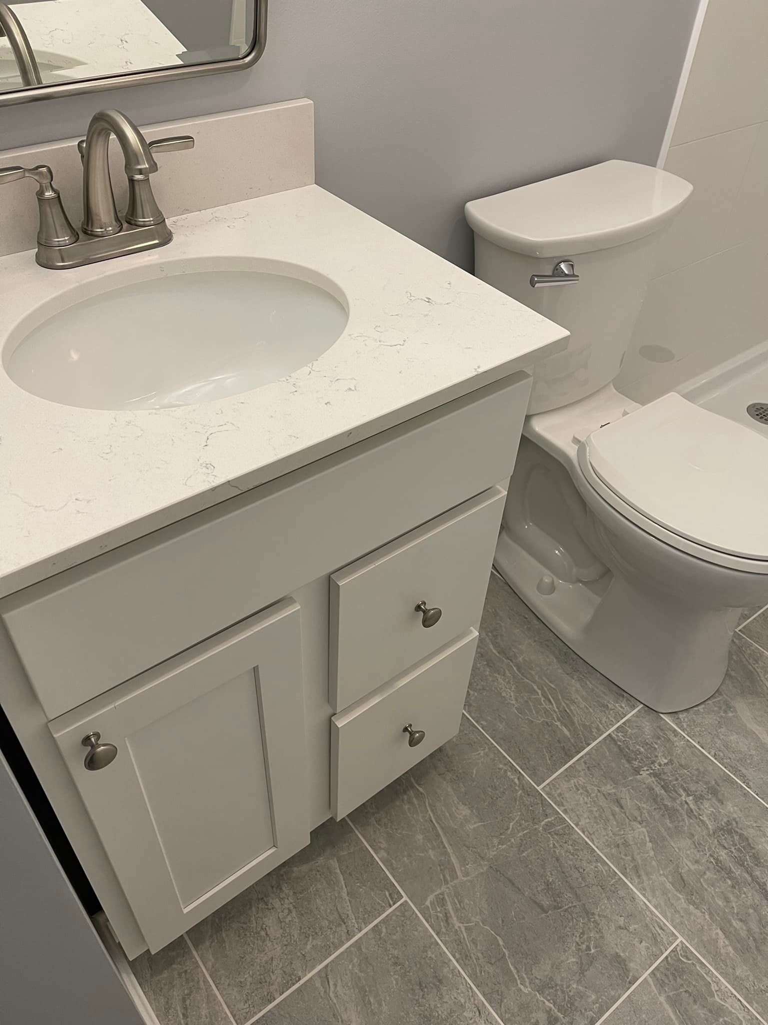 Bathroom with white vanity, sink, faucet, and toilet; grey floor and walls.