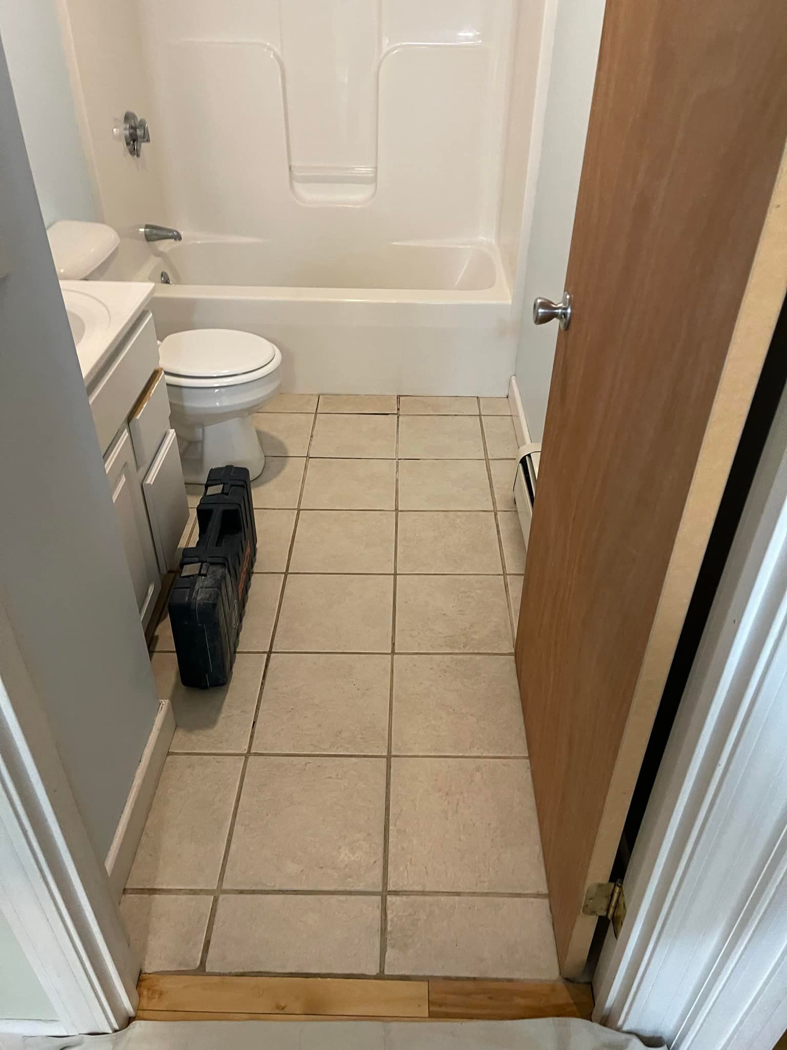 Bathroom with tile floor, white tub and toilet. Open door frame to the right.