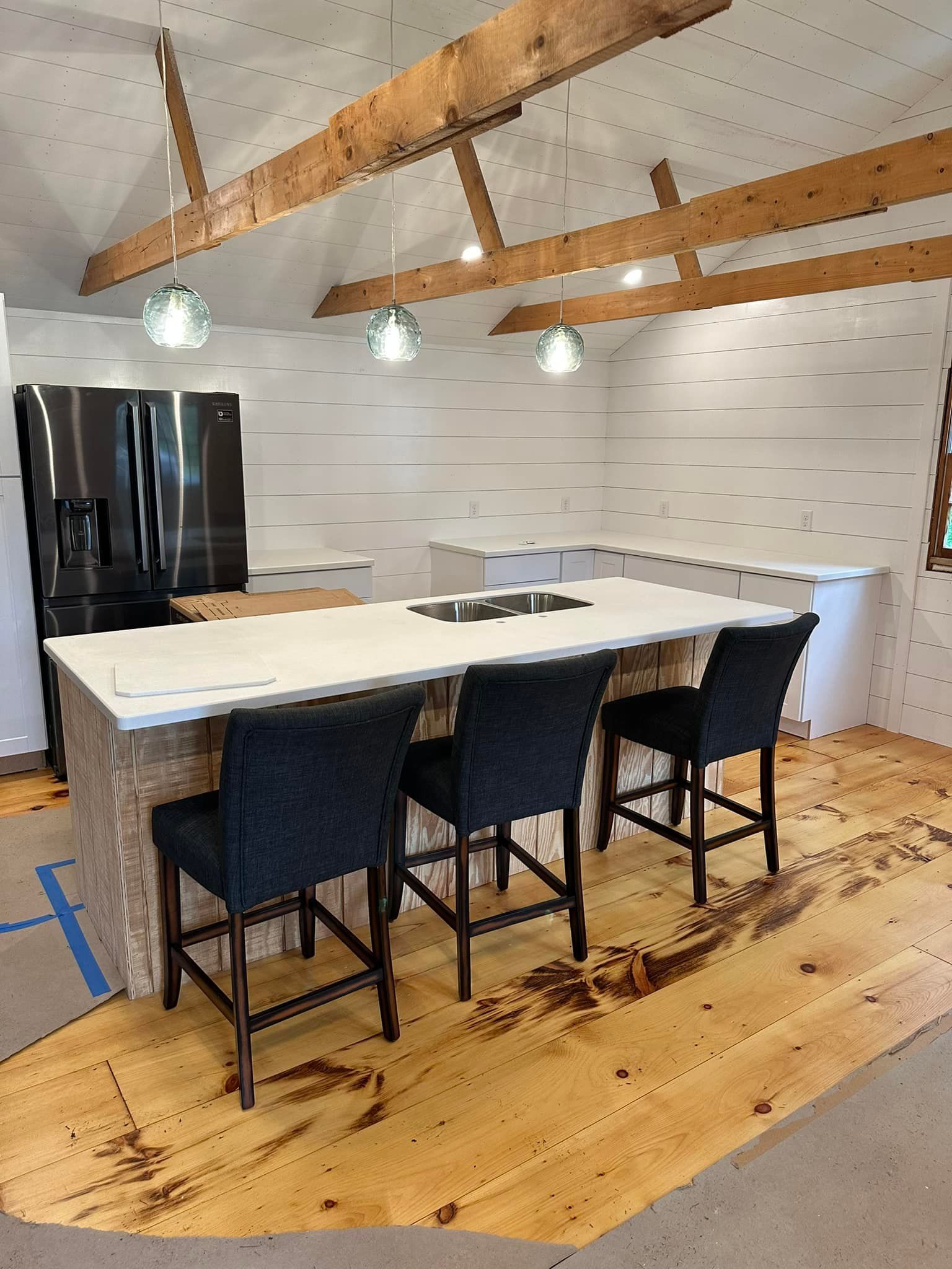Modern kitchen with island, three bar stools, stainless steel appliances, wood beams.
