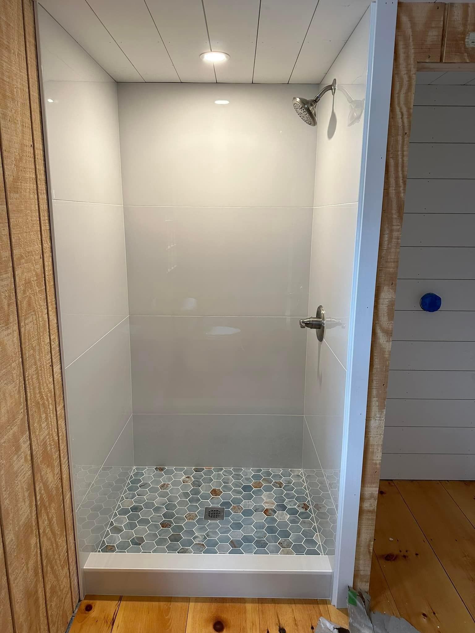 Shower stall with blue tiled floor, white walls, and silver fixtures, partially framed.
