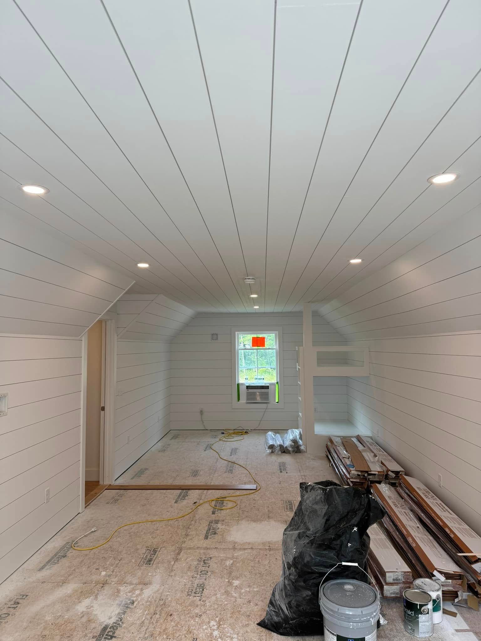 Interior room under construction with white paneled walls and ceiling, recessed lights, and a window.