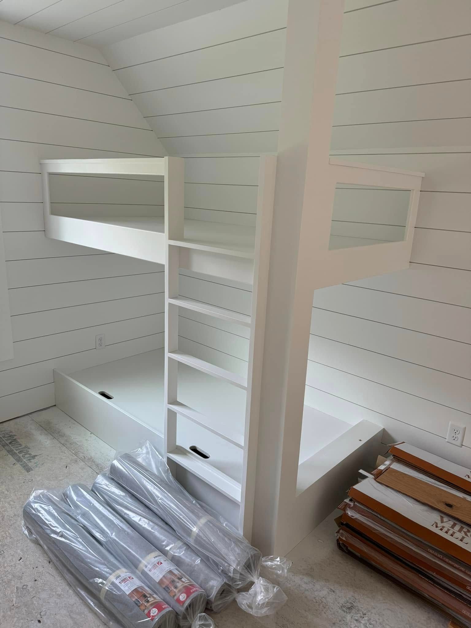 White bunk bed with shelves against white plank walls, rolls of rugs on the floor.