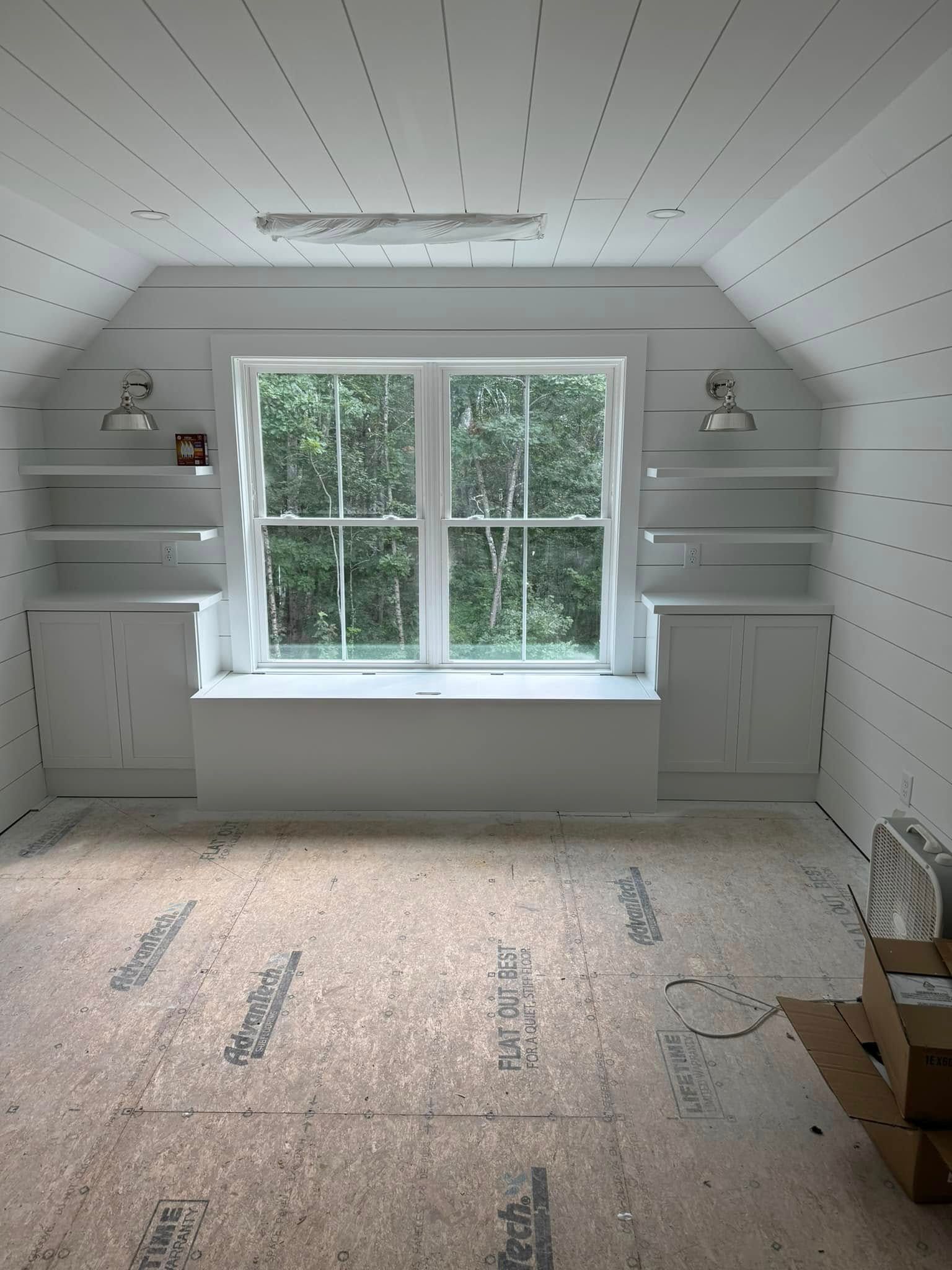 White attic room with window, built-in cabinets, and shelves. Unfinished flooring.