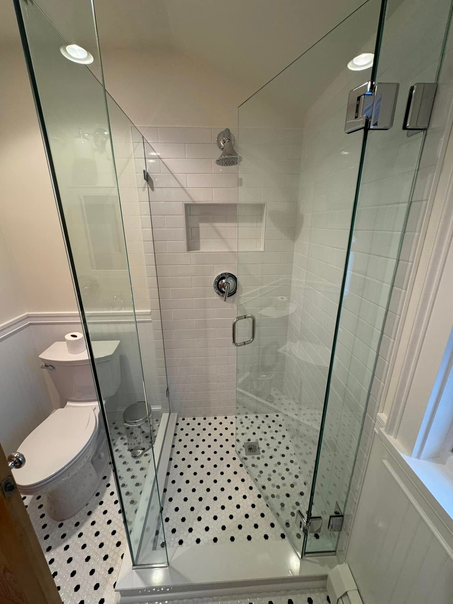 A modern bathroom with a glass shower, white and black tile, and a toilet.