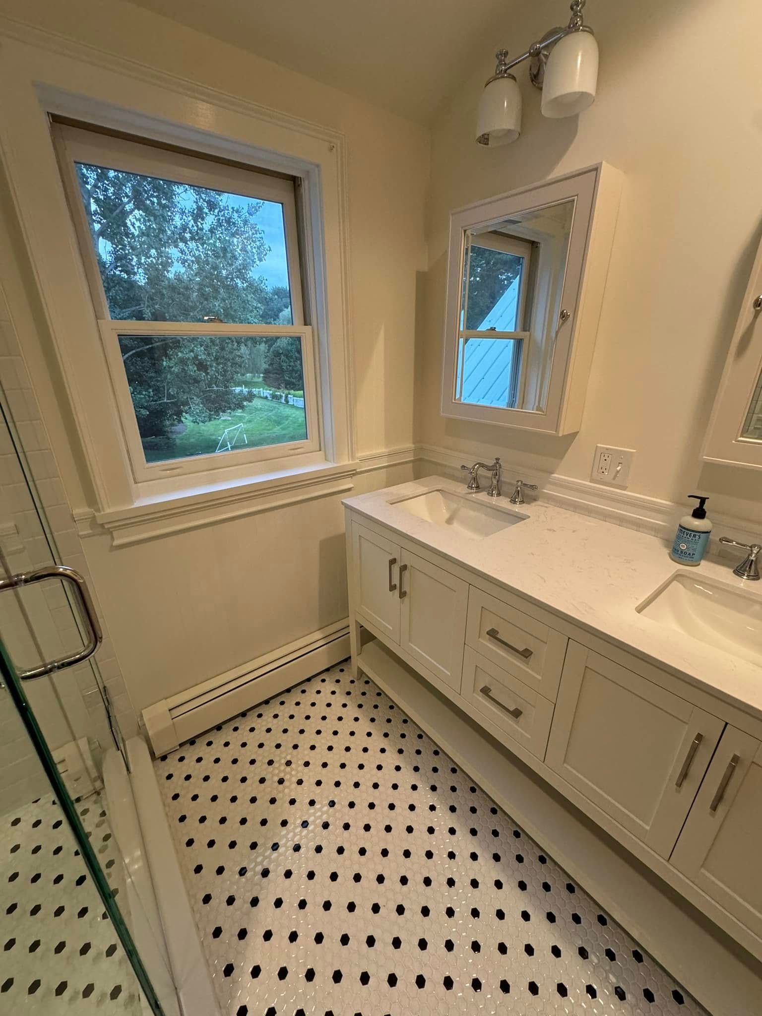 Bathroom with white vanity, black and white tiled floor, two sinks, and windows.