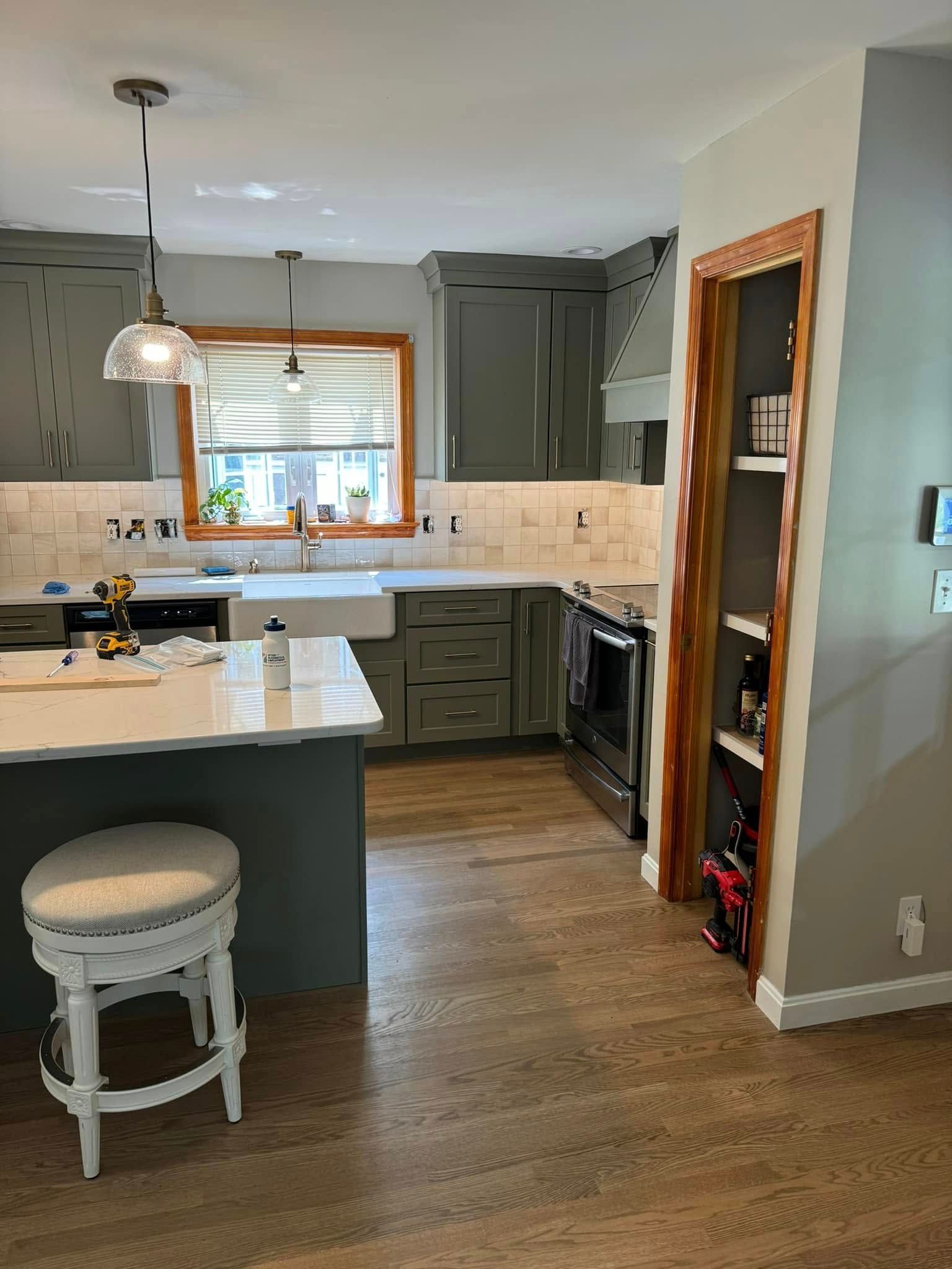 Kitchen with green cabinets, white countertops, and wood floors; a bar stool sits at the island.