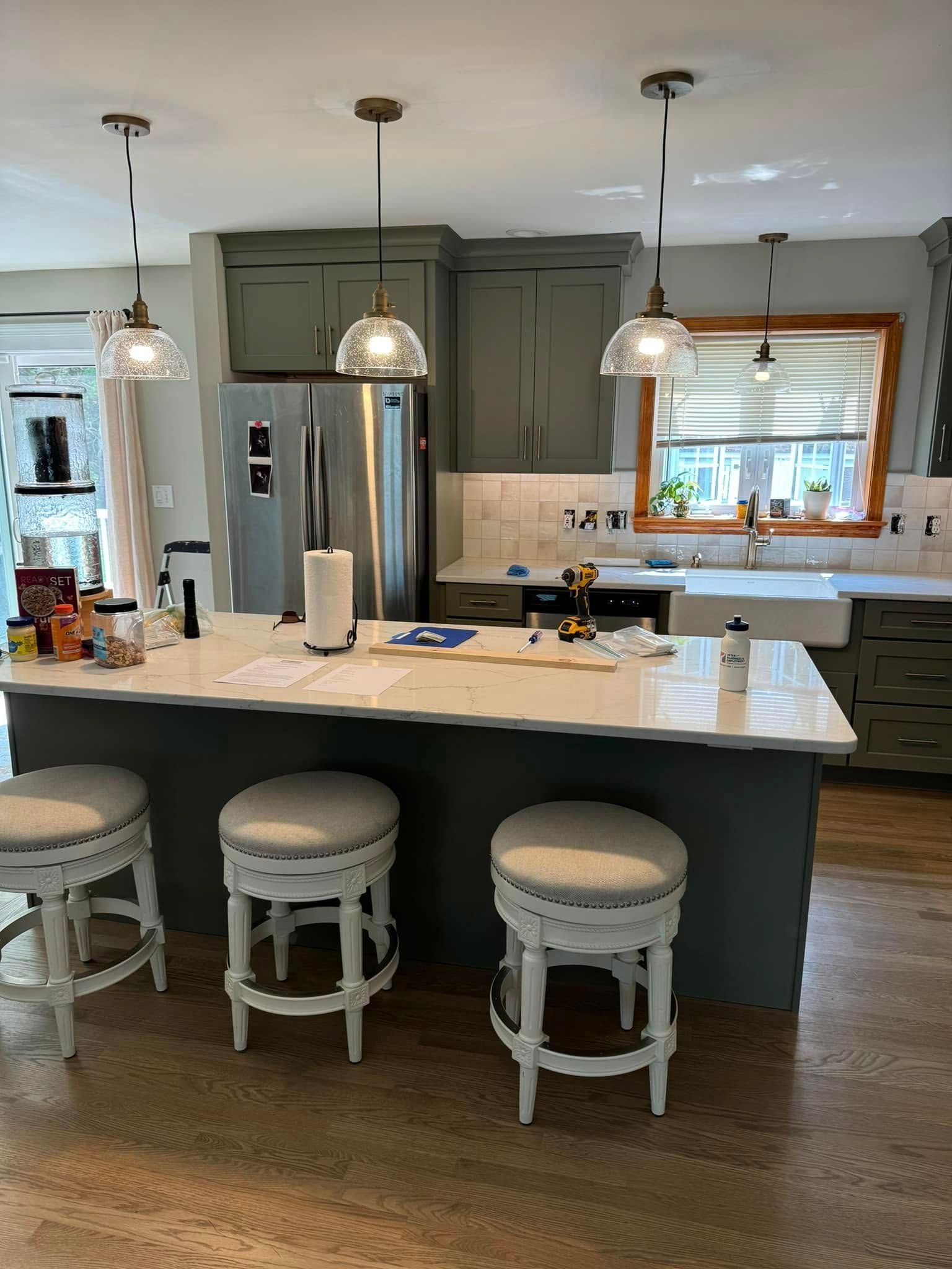 Kitchen with green cabinets, white countertops, and stools; pendant lights hang over an island.