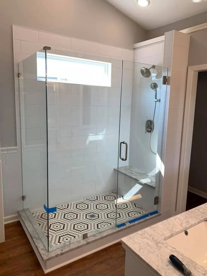 Glass-enclosed shower with white tile walls, black and white geometric floor tile, and a built-in bench.