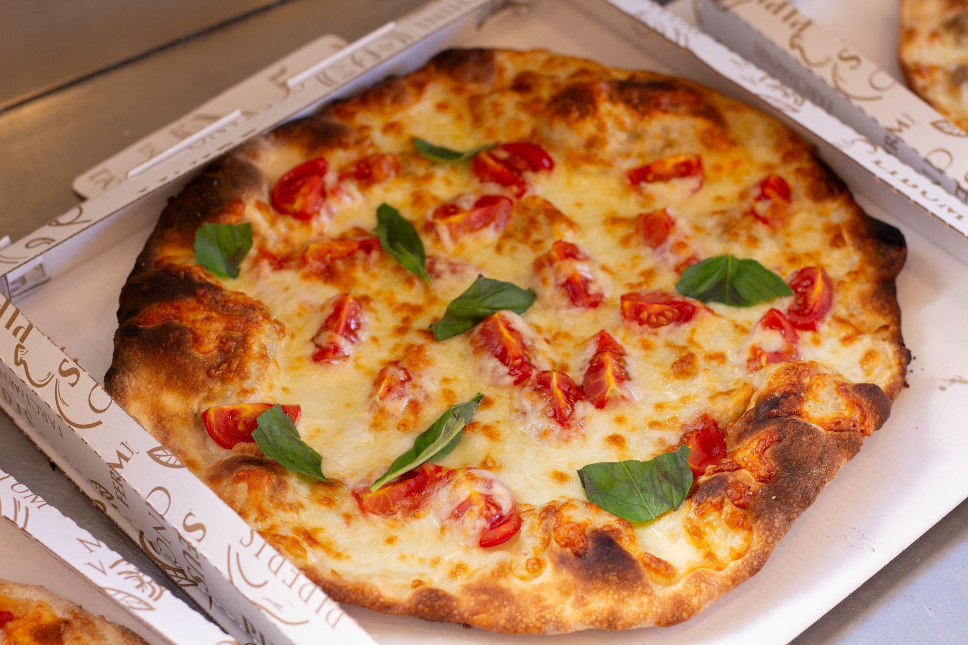 Pizza in una scatola di cartone, condita con pomodori e basilico.