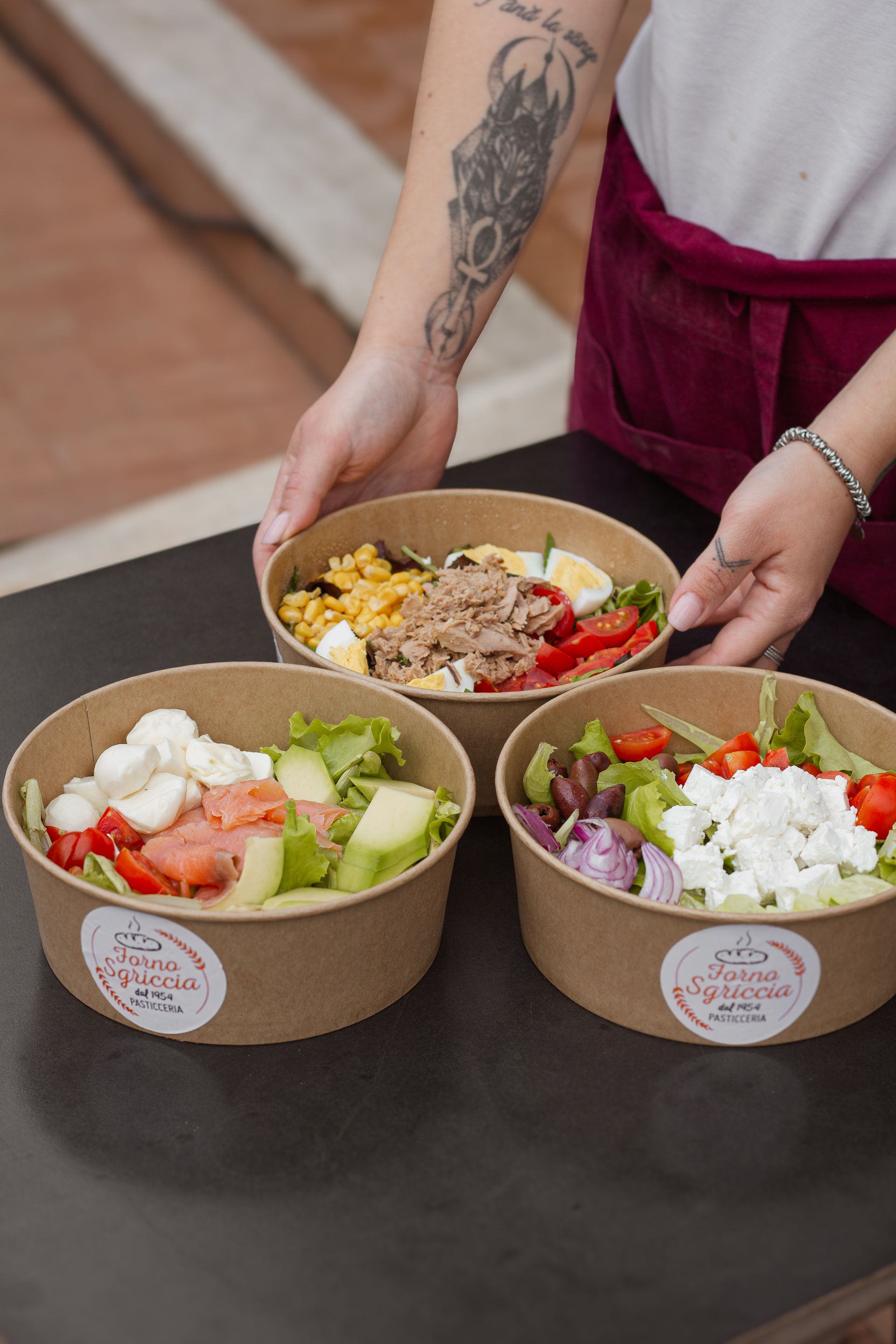 Persona che tiene in mano tre insalatiere con vari ingredienti su un tavolo.