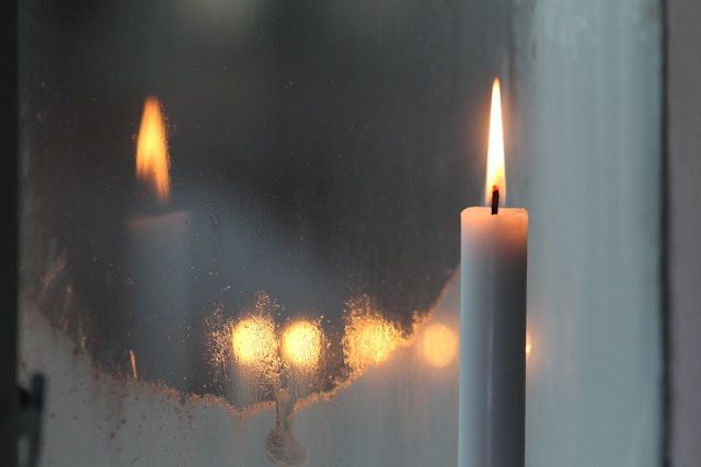 Single lit candle by window with soft reflections, symbolizing remembrance, cremation services Middl