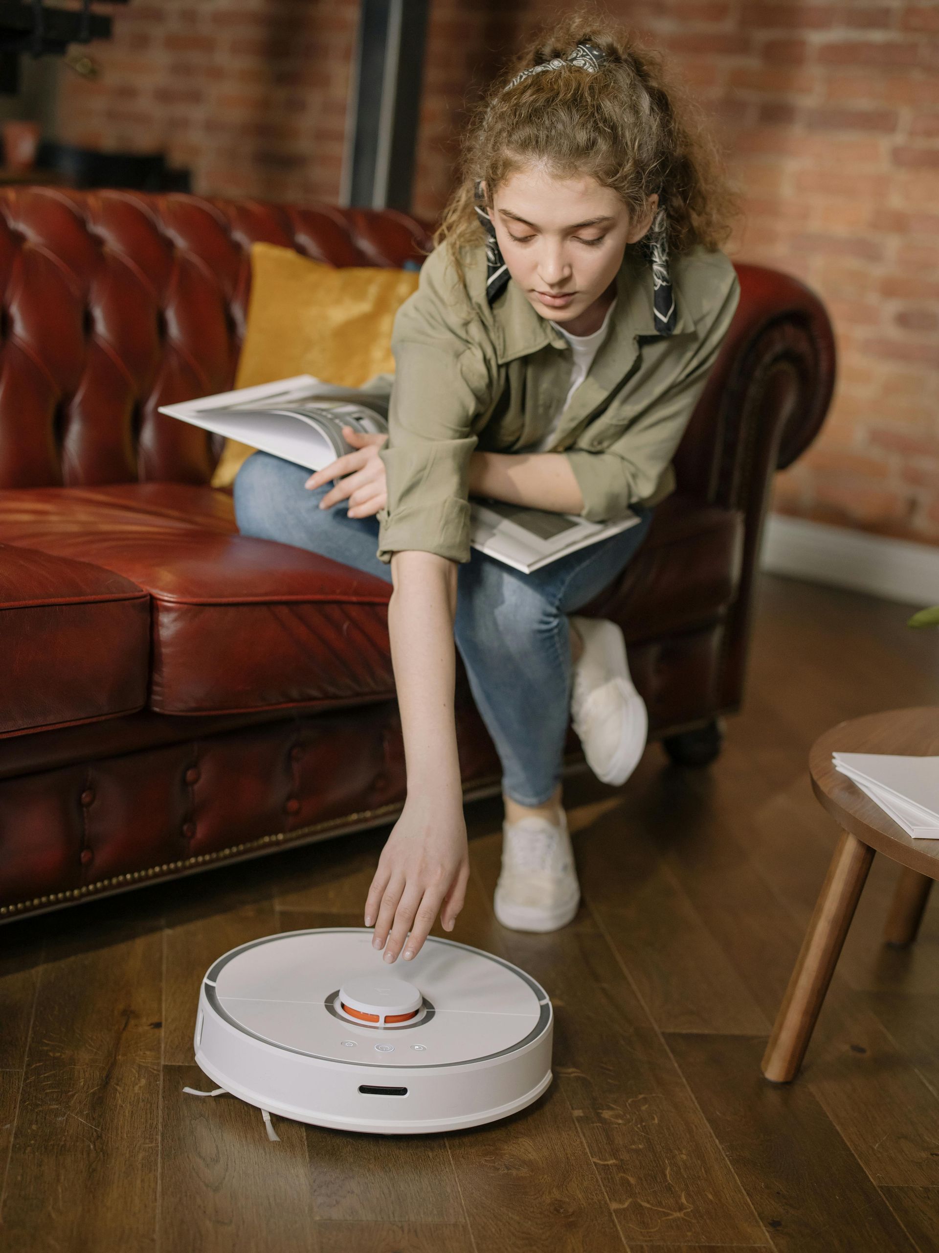 A woman is sitting on a couch using a robot vacuum cleaner.