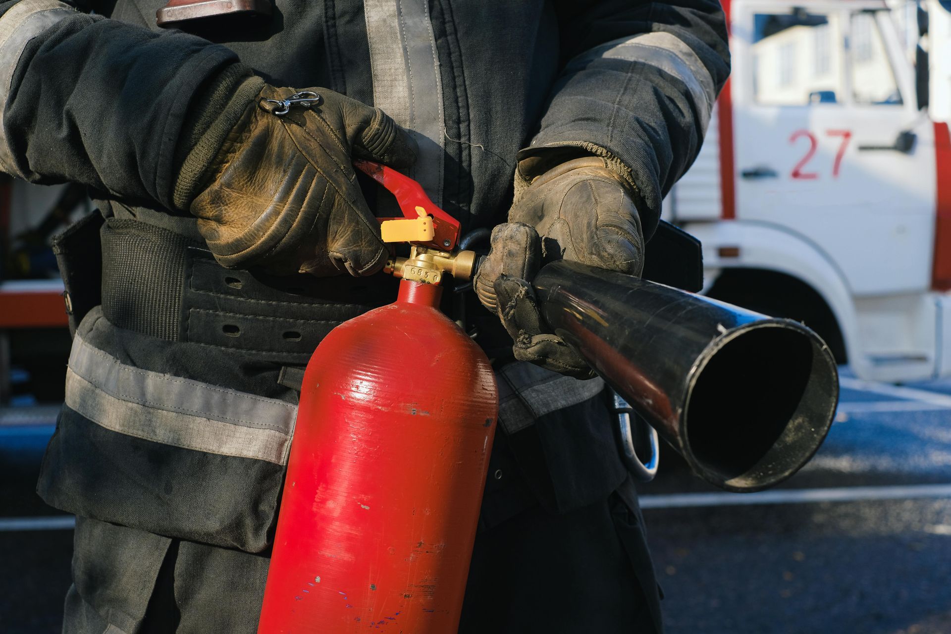 A fireman is holding a red fire extinguisher in front of a fire truck.