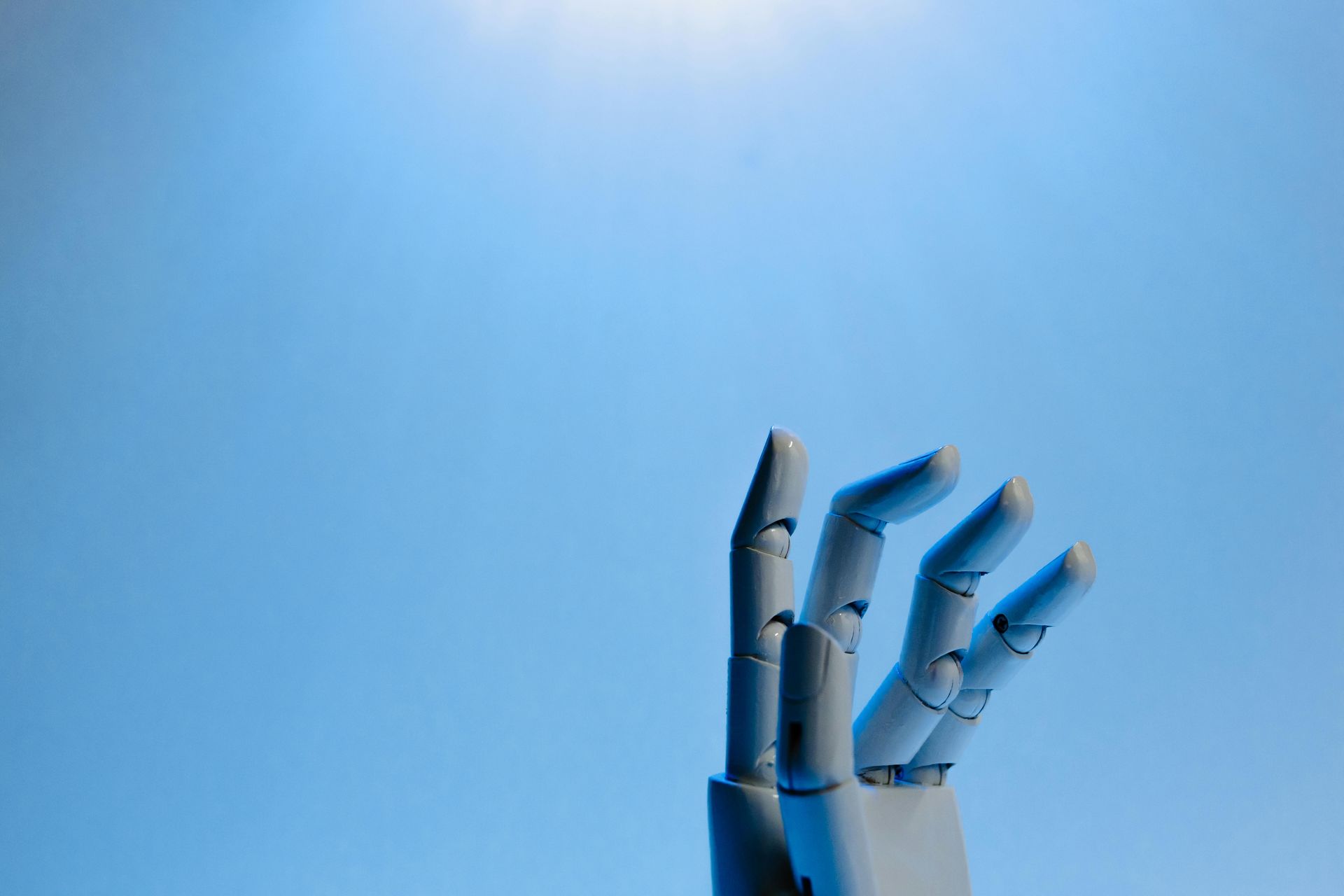 A close up of a robotic hand against a blue sky.