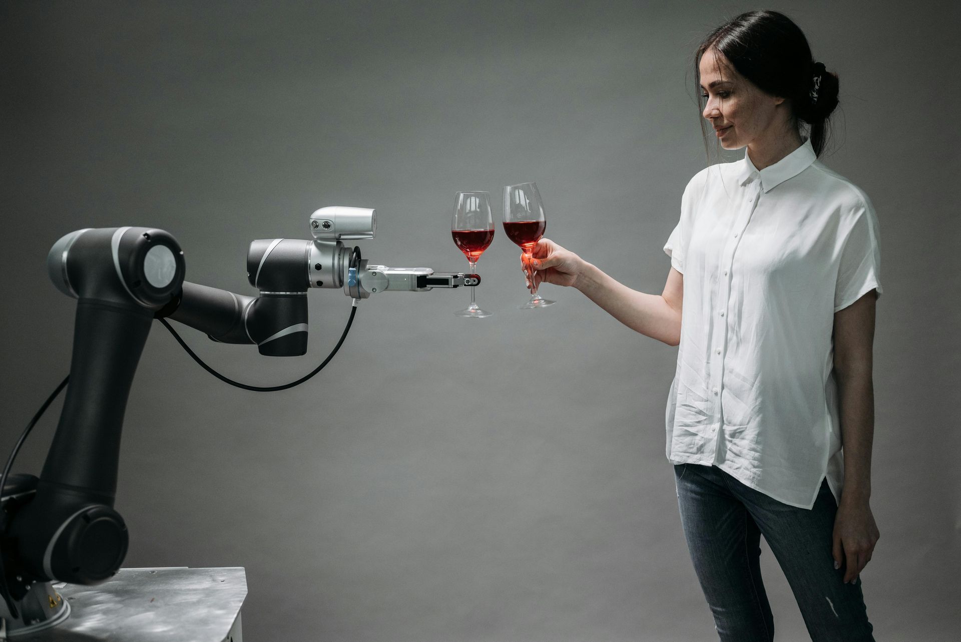 A woman is holding two glasses of wine in front of a robotic arm.