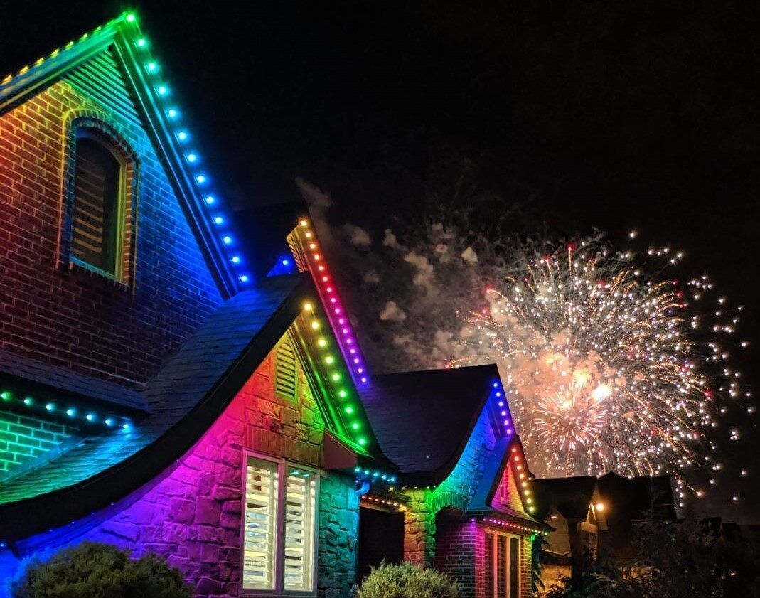 A house is lit up with rainbow lights and fireworks are going off in the background.