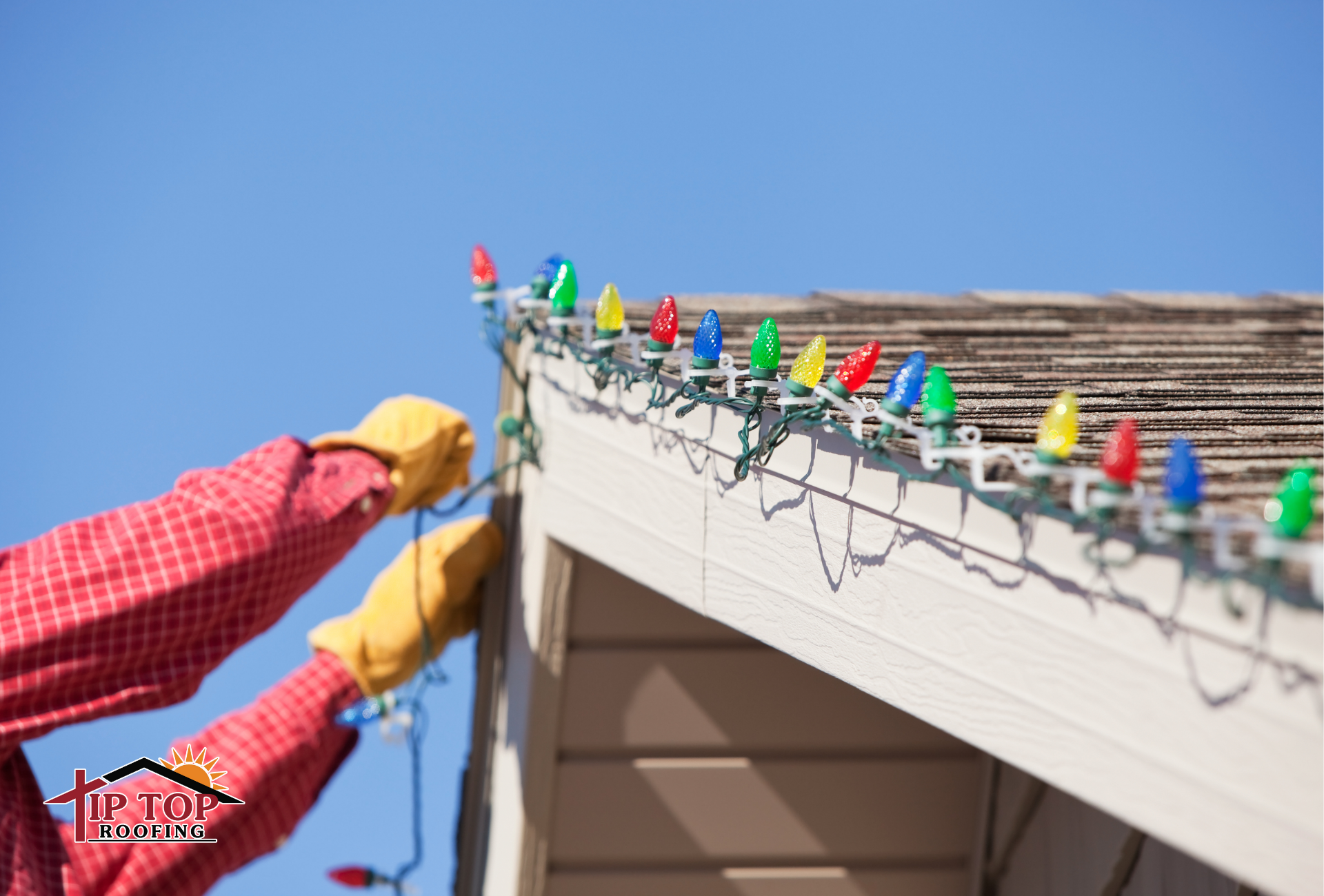 A man installing Christmas lights on a shingle roof using plastic clips to safely decorate his home.
