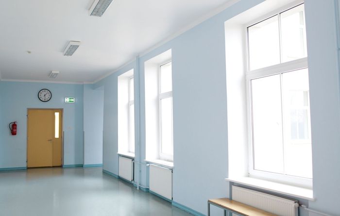 Un couloir vide avec des murs bleus et des fenêtres blanches.