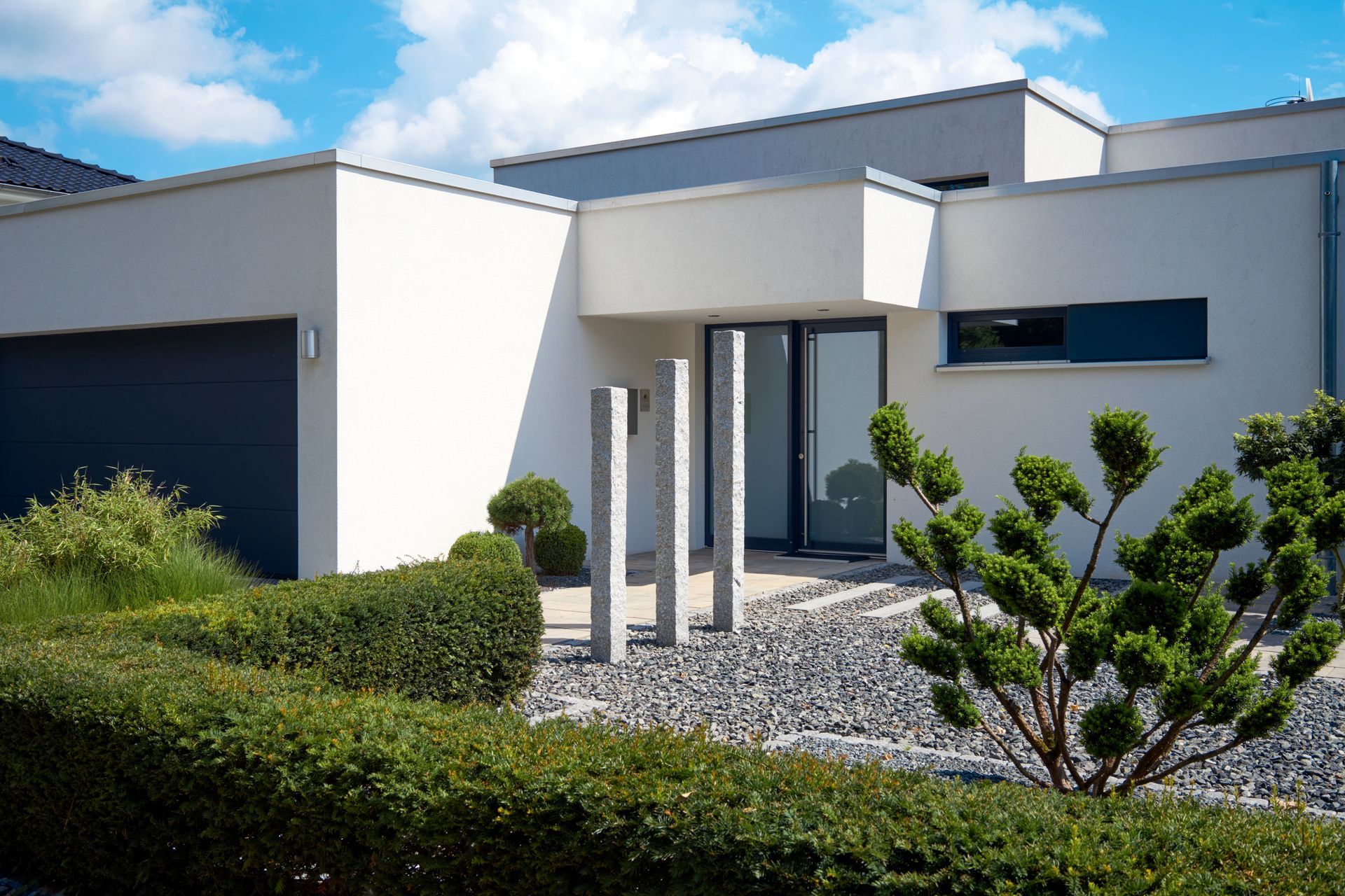 Une maison blanche moderne avec un garage et un buisson devant