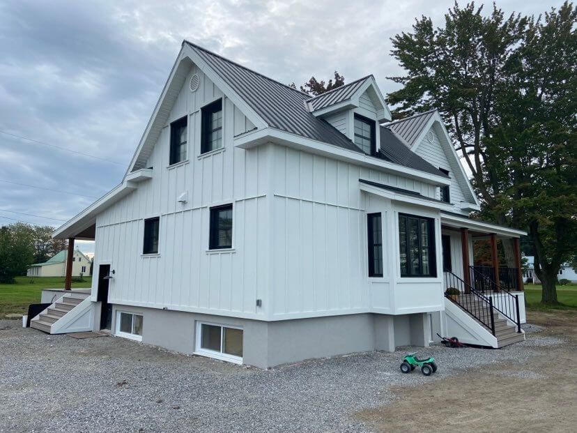 Une maison blanche avec un toit noir et un tracteur jouet vert devant elle