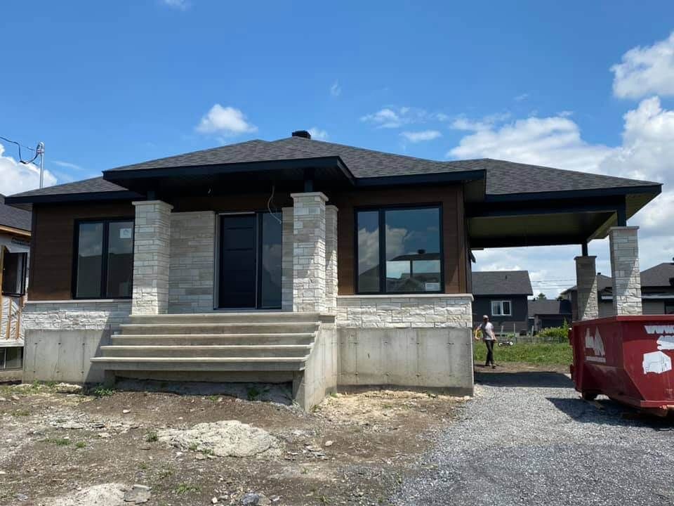 Une maison en construction avec une benne à ordures devant.