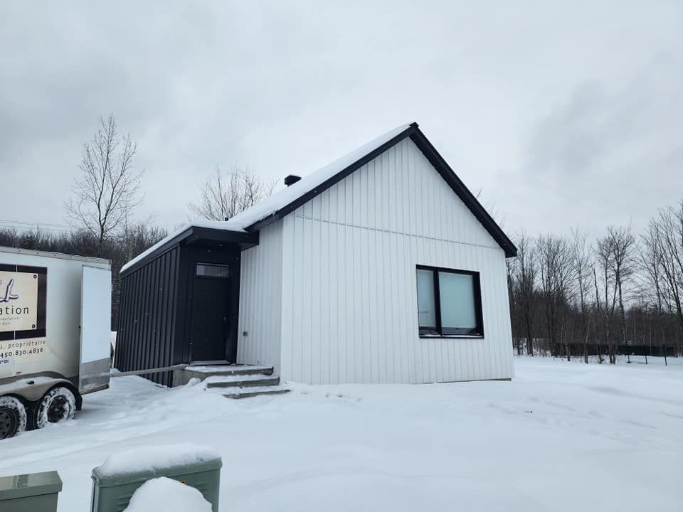 Une petite maison blanche avec une caravane attachée dans la neige.