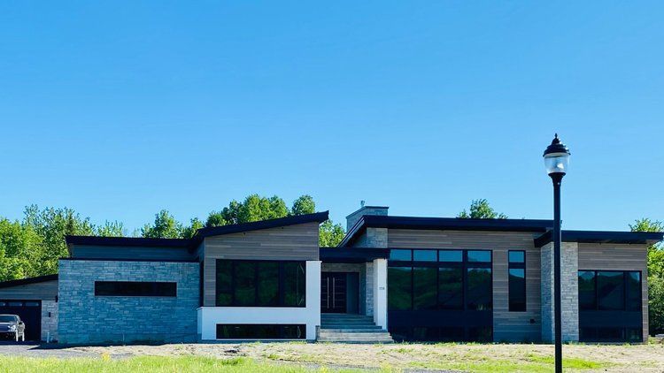 Une grande maison avec beaucoup de fenêtres est située au sommet d'un champ verdoyant.