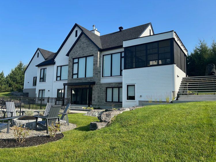 Une grande maison blanche avec beaucoup de fenêtres est située au sommet d'une colline verdoyante.