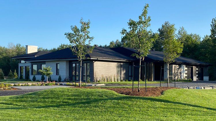 Une grande maison avec beaucoup de fenêtres est entourée d'arbres et d'herbe.
