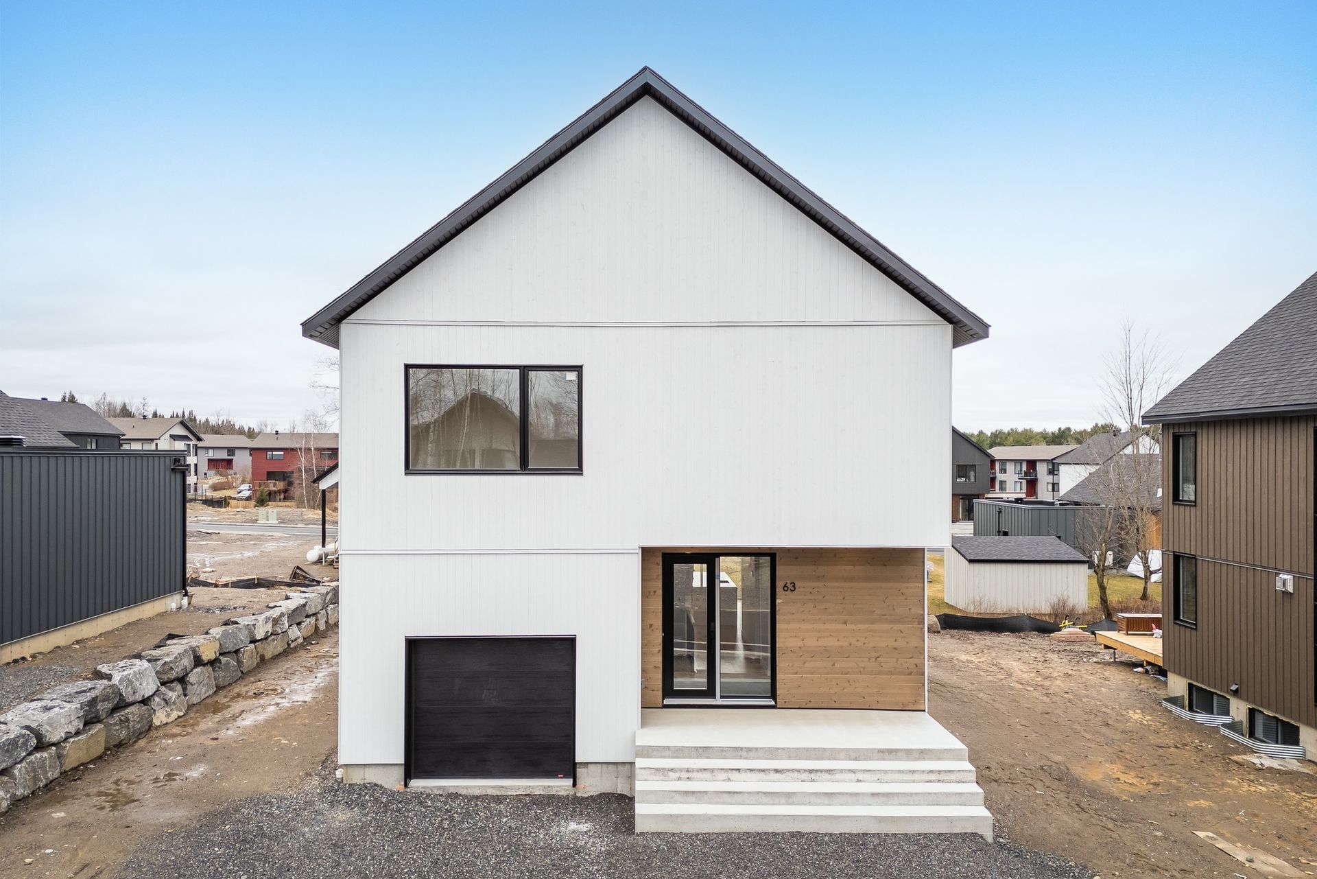 Une maison blanche avec un toit noir est assise au sommet d'un champ de terre.