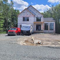Un camion rouge et une remorque sont garés devant une maison en construction.