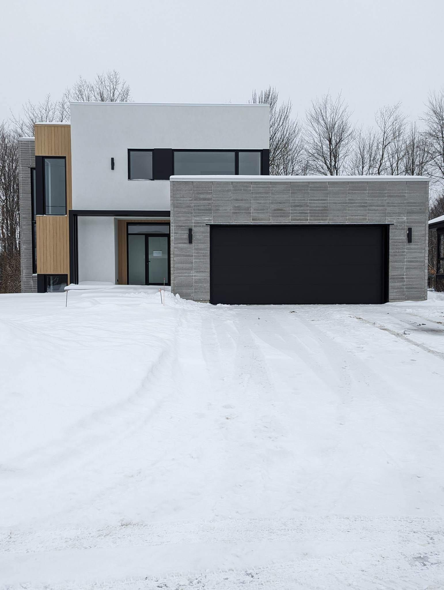 Une maison moderne avec une porte de garage noire est recouverte de neige.