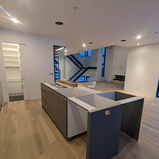 Une cuisine avec un grand îlot et des escaliers en arrière-plan.