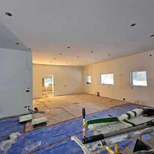 Une grande pièce avec une bâche bleue sur le sol est en cours de rénovation.