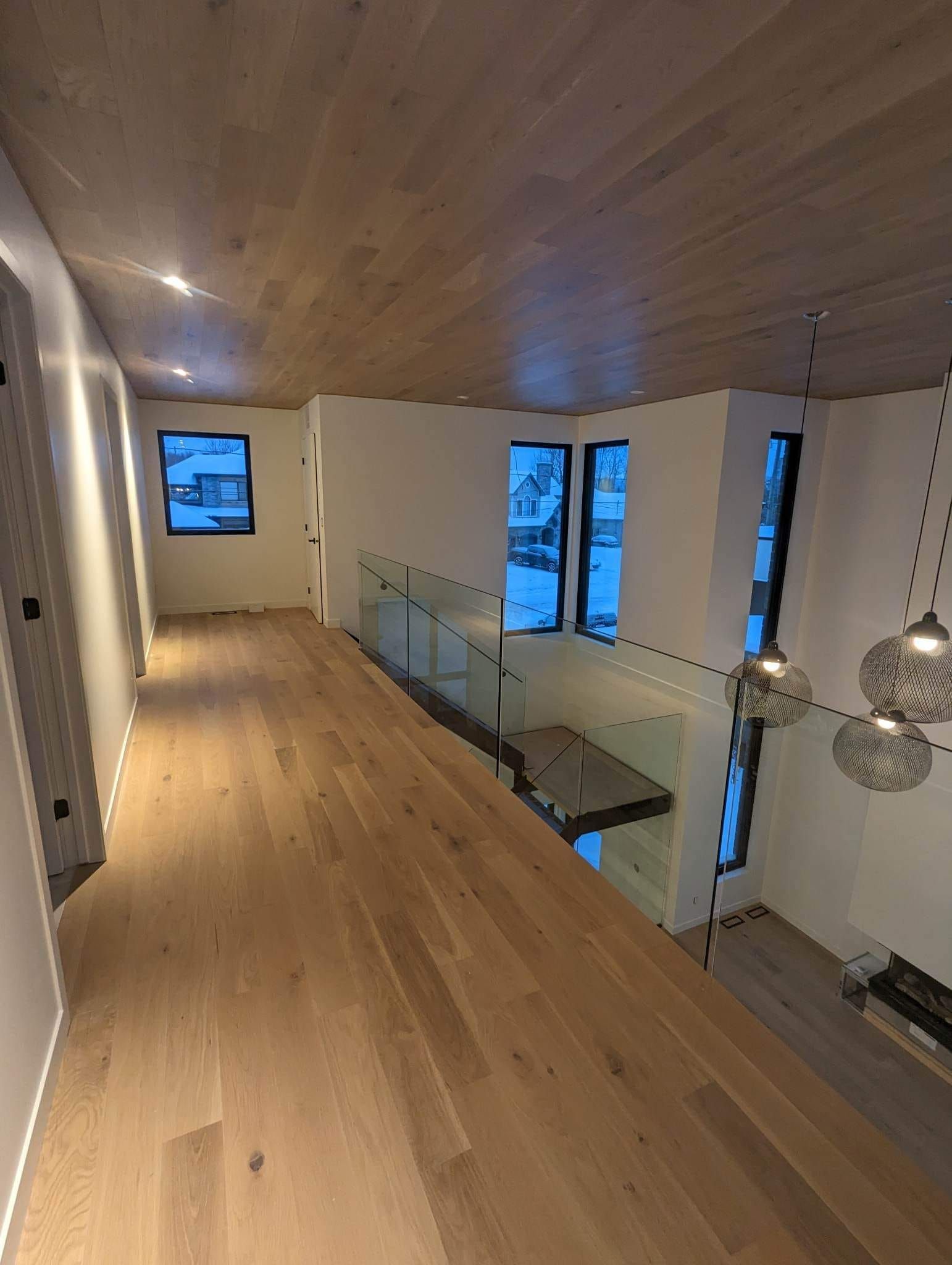 Un couloir dans une maison avec du parquet et une balustrade en verre.